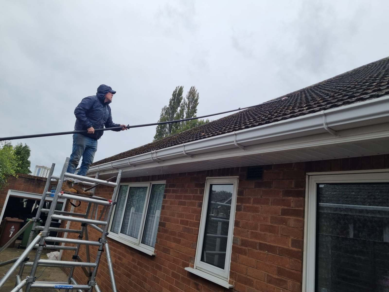 Operative using a long-reach pole to clear moss from a tiled roof