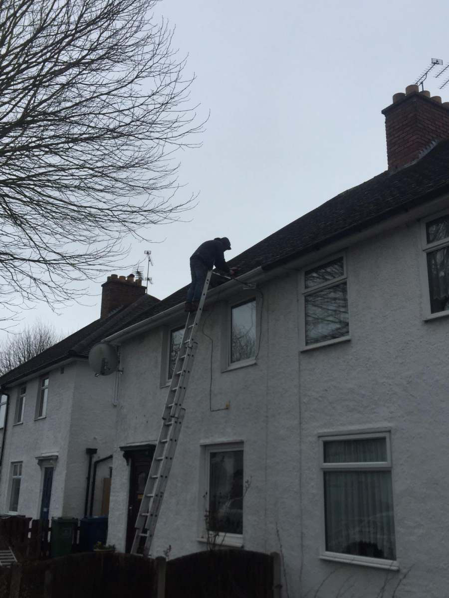 Roofer on a ladder repairing the gutter line of a rendered semi-detached house