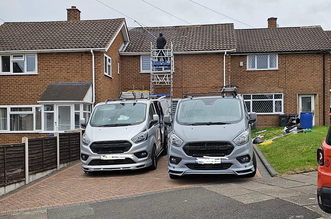 Two GS Roofs Ltd vans on a driveway with roofers on scaffolding