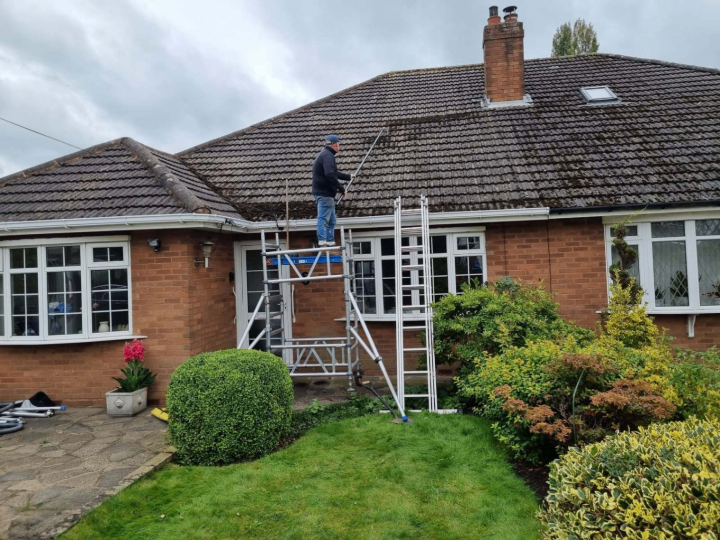 Telescopic soft-wash pole clearing moss from a weathered UK roof