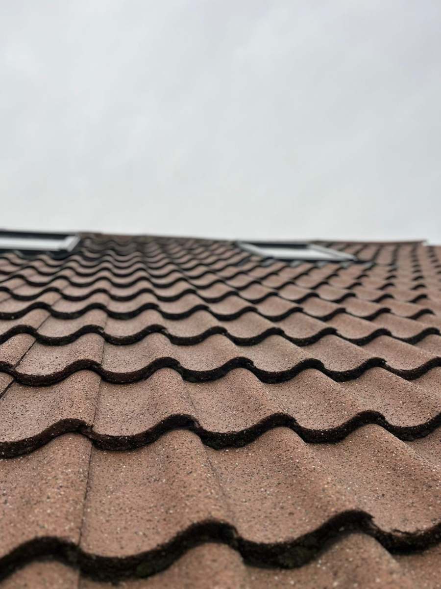 Close-up of freshly cleaned reddish-brown pantile roof with skylights against an overcast Staffordshire sky