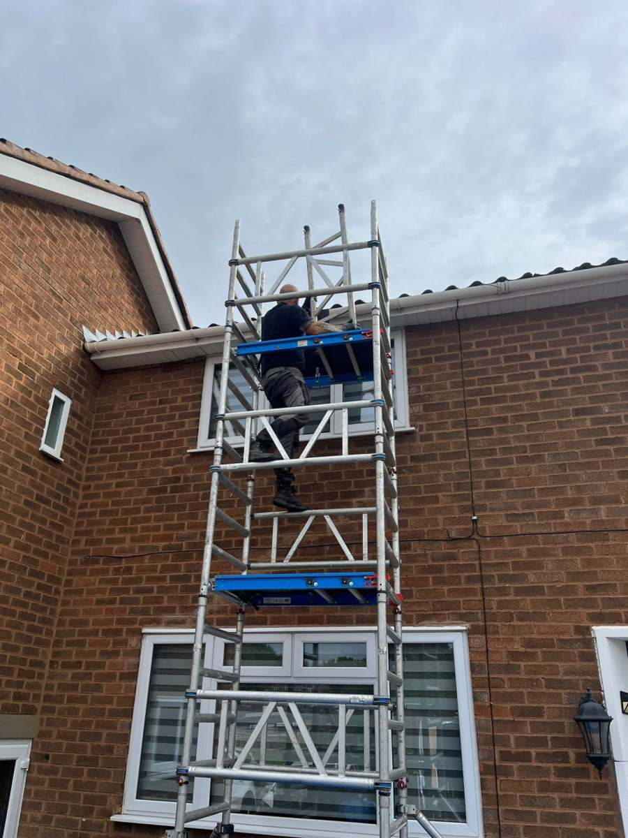 GS Roofs operative on a tall scaffold tower reaching the roofline