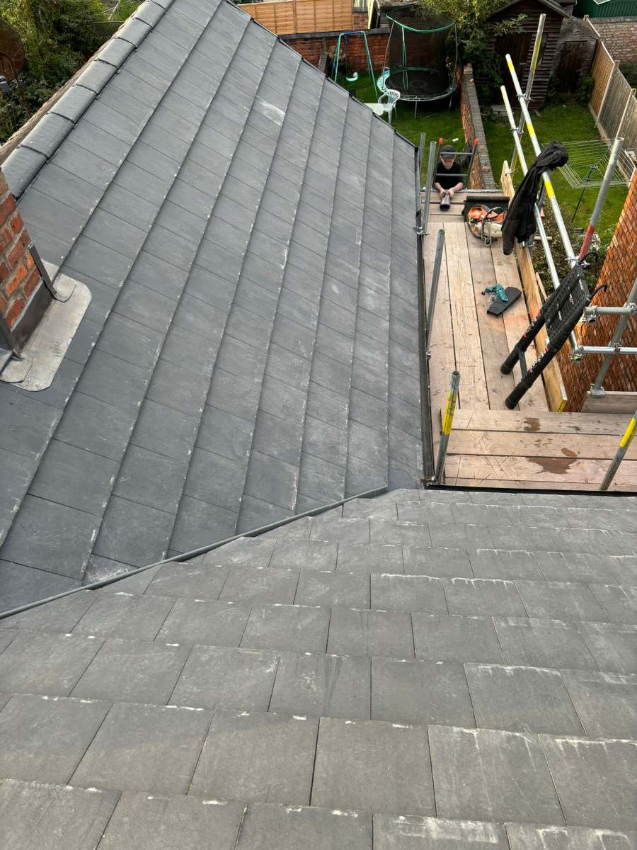 Freshly laid slate-grey tiles on a new pitched roof beside GS Roofs scaffolding