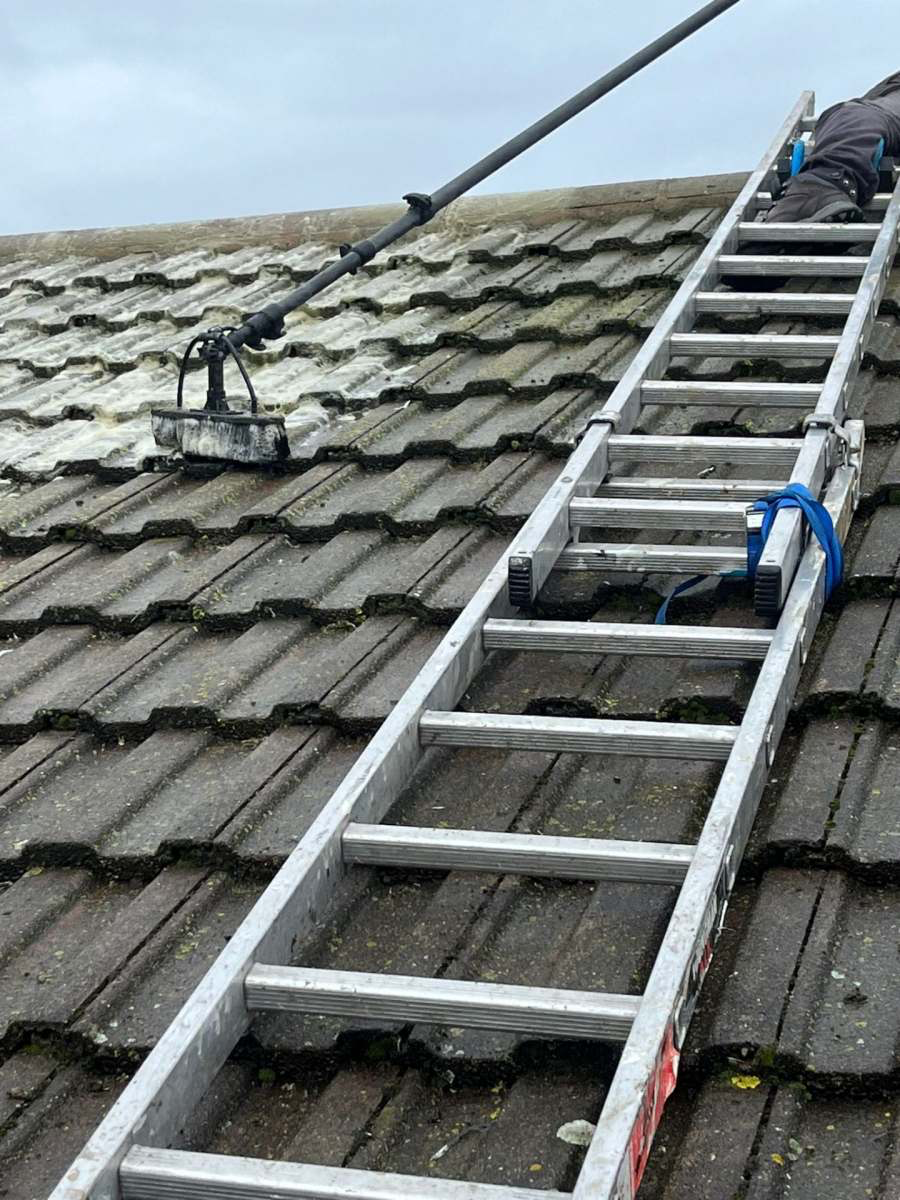 Operative using a low-pressure cleaning tool during a soft-wash roof clean
